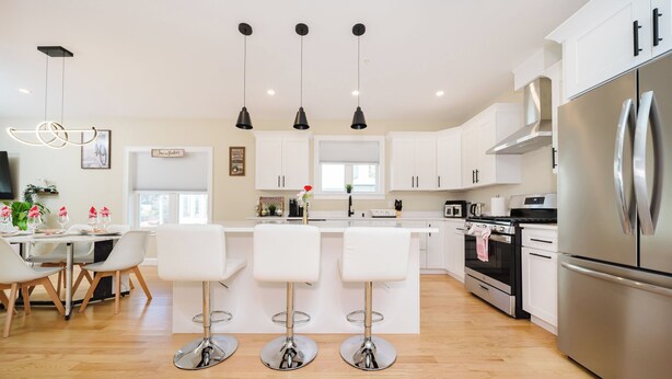 Una cocina moderna con armarios blancos, electrodomésticos de acero inoxidable y una isla central con taburetes de bar.