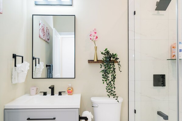 Un baño moderno con lavamanos blanco, espejo, inodoro y zona de ducha.