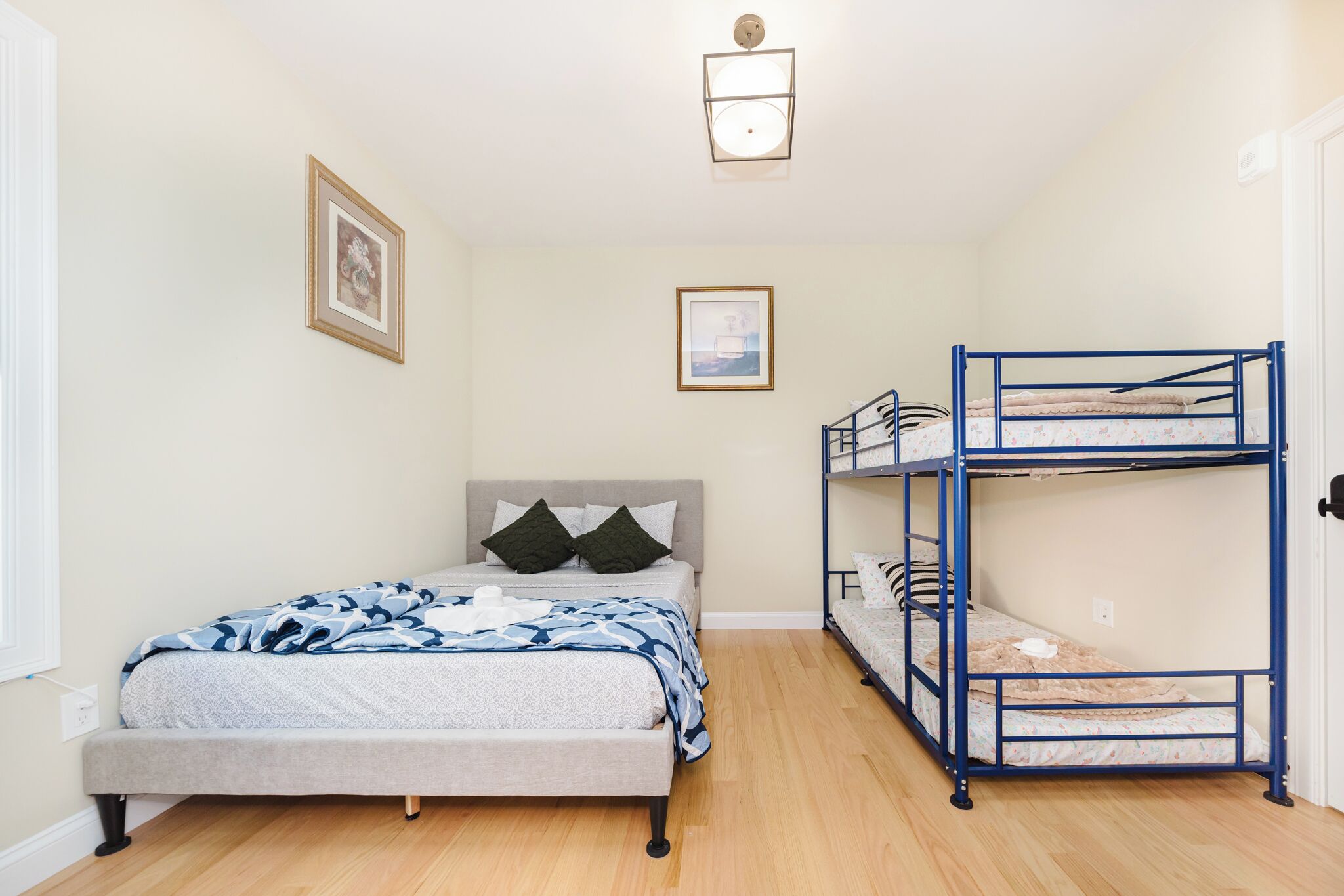 A bedroom with a single bed, a bunk bed, light-colored walls, and a ceiling light fixture.