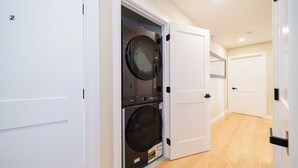 Un lavadero con dos lavadoras y secadoras apiladas, puertas blancas y suelo de madera.