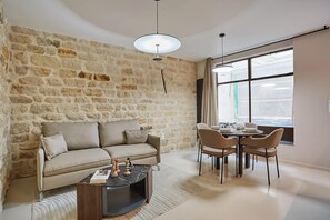 A living room with a stone wall, a sofa, a coffee table, and a dining area with chairs and a table. - Apartment Center of Paris (Paris)