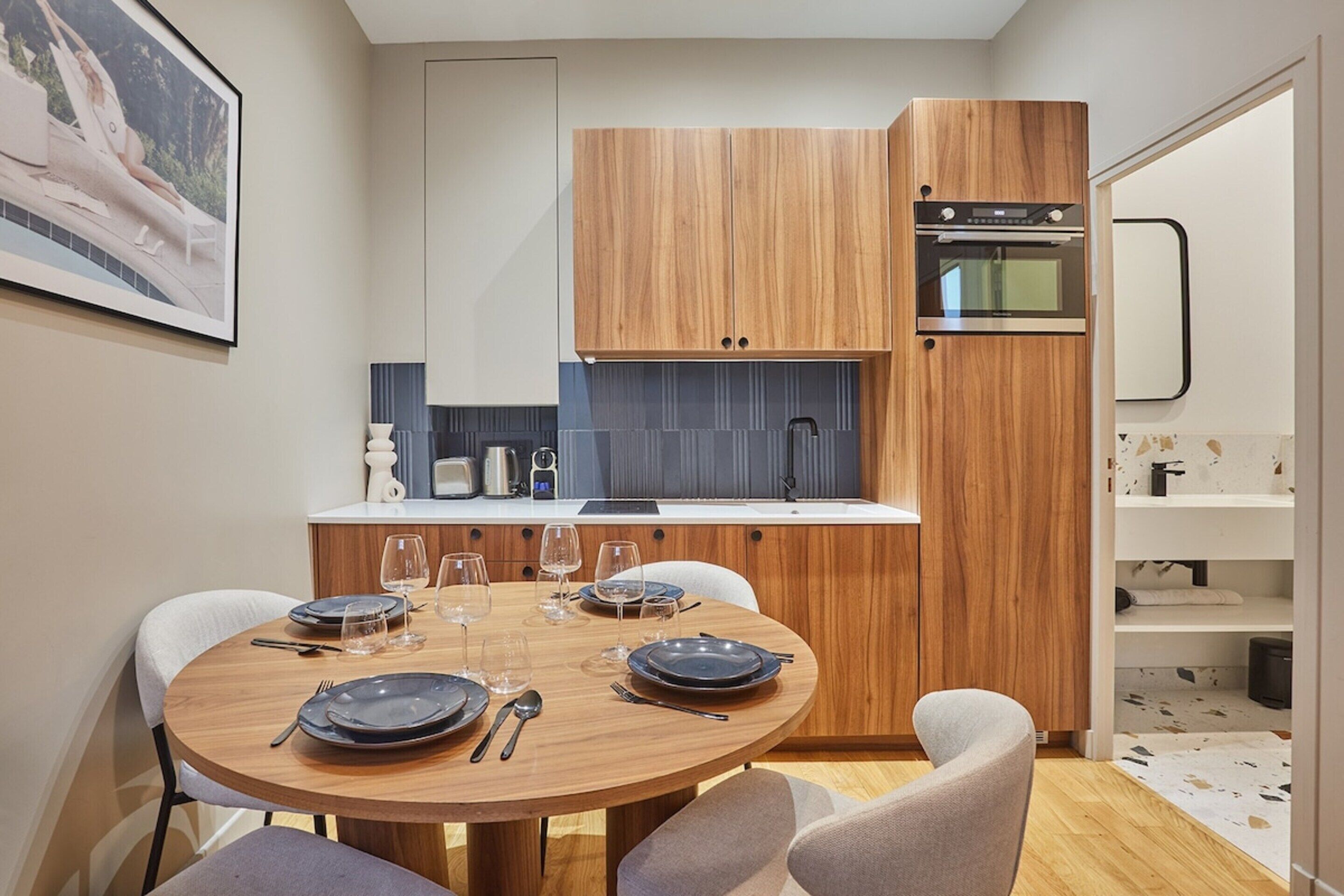 A modern kitchen with wooden cabinets, a built-in oven, and a dining area with a round table set for four.