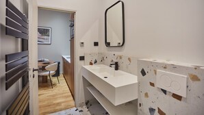 Ein modernes Badezimmer mit einem weißen Waschbecken, einem großen Spiegel und einer Holztür, die in einen Essbereich führt.