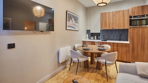 Eine moderne Küche mit Holzausstattung, ein Essbereich mit rundem Tisch und Stühlen, ein Flachbildfernseher an der Wand und eine Pendelleuchte über dem Esstisch.