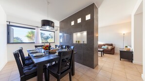 A modern kitchen with a dining area, large windows, and a living room with a sofa and a lamp. - Townhouse w/ Pool and BBQ in Albufeira (Albufeira)