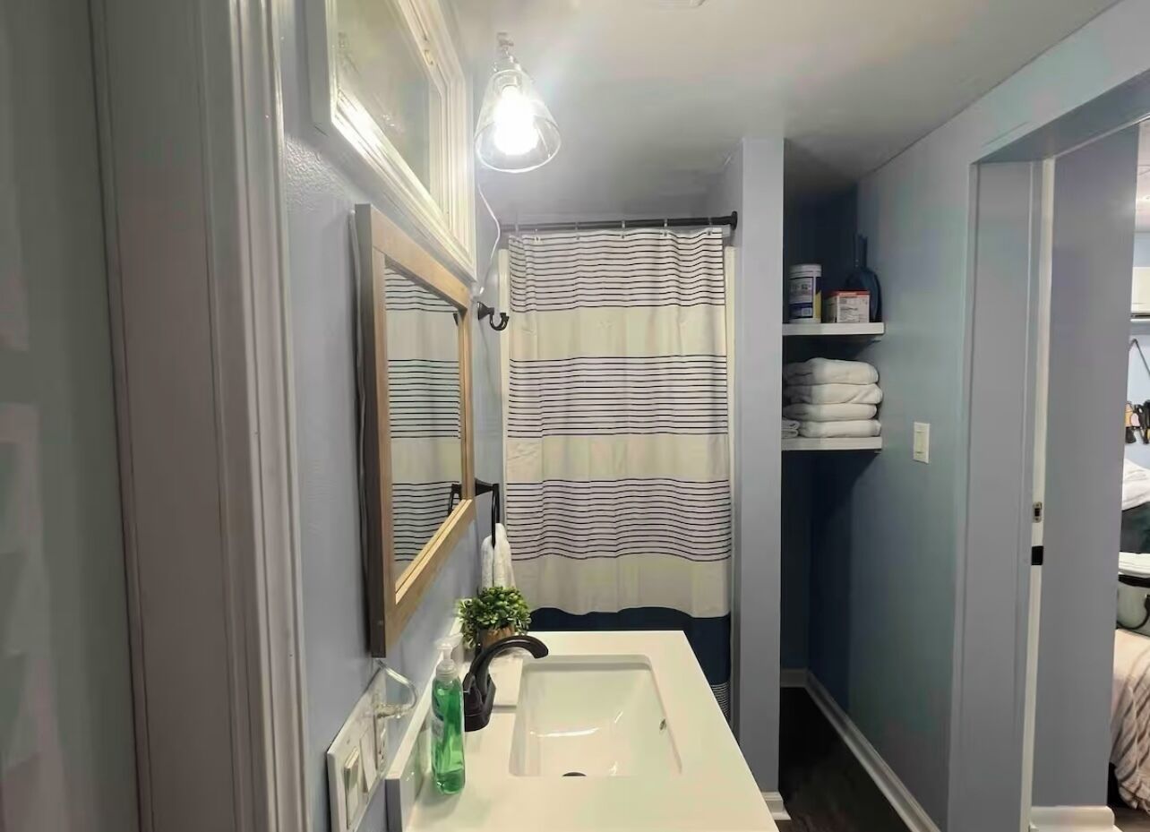 A bathroom with a white sink, a mirror, a striped shower curtain, and a shelf with towels.