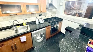 A modern kitchen with wooden cabinets, a stainless steel sink, a built-in oven, a gas stove, and a window offering a city view. - Luxury two bedroom skyline views apartment/Flat (Birmingham)