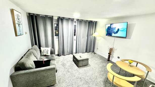A modern living room with a grey sofa, a small round table with yellow chairs, and a TV mounted on the wall. - Luxury two bedroom skyline views apartment/Flat (Birmingham)