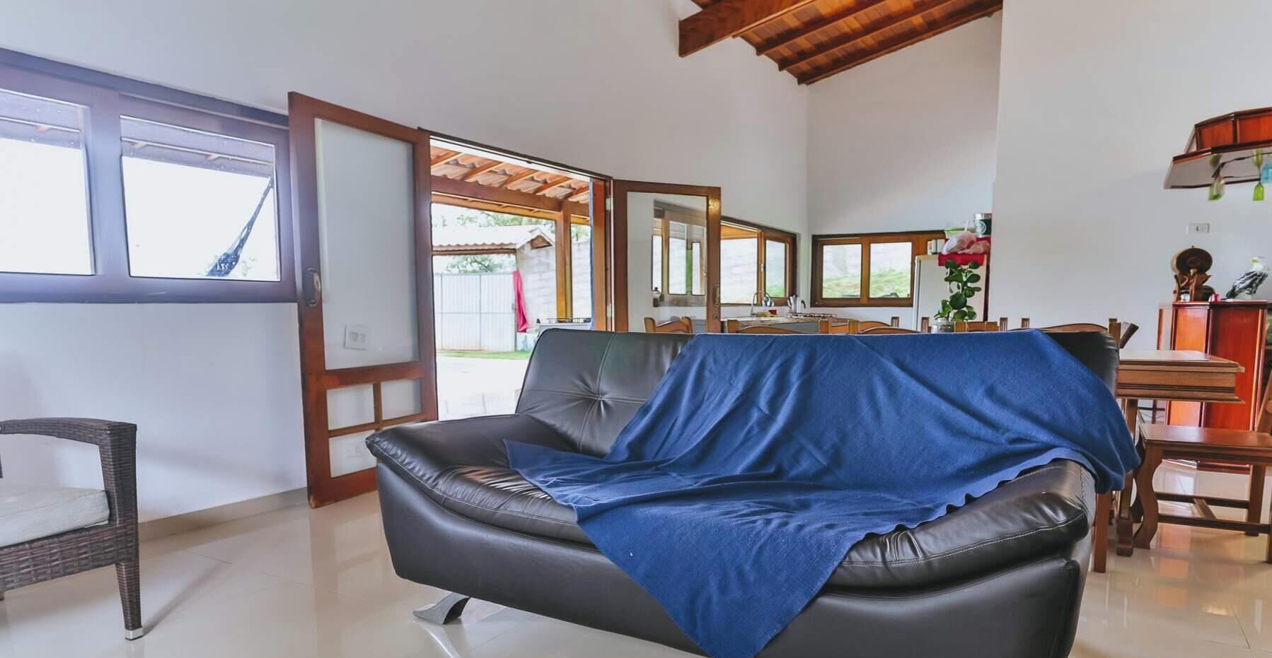 Ein Wohnzimmer mit schwarzem Ledersofa, einem Essbereich mit Holztisch und -stühlen sowie einem Blick durch eine Glastür ins Freie.