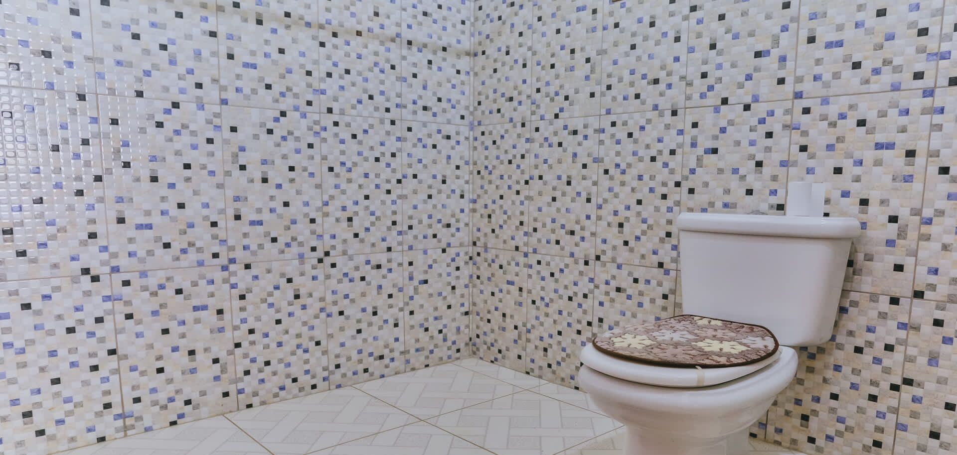 Een badkamer met wandtegels in mozaïek en een toilet met een decoratief zitje.