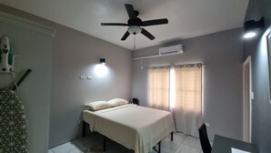 A bedroom with a bed, ceiling fan, air conditioning unit, and a window with curtains. - Rest Easy Suite #1 with Mountain and Sea Views (Spooners Village, Cayon)