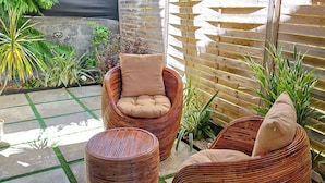A covered outdoor seating area with wicker furniture, a concrete floor, and a wooden fence. - The nice corner (Grand baie)