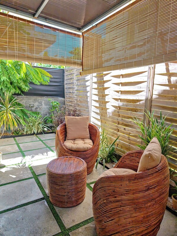 A covered outdoor seating area with wicker furniture, a concrete floor, and a wooden fence.