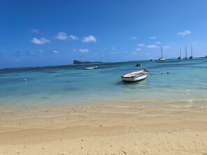 A beach with clear turquoise water, a sandy shore, and several boats anchored in the distance.