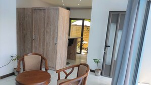 A room with a wooden wardrobe, two wooden chairs, a round wooden table, and a small potted plant. - The nice corner (Grand baie)
