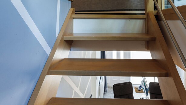Una escalera de madera con barandilla de metal que da a una habitación con vistas al exterior.