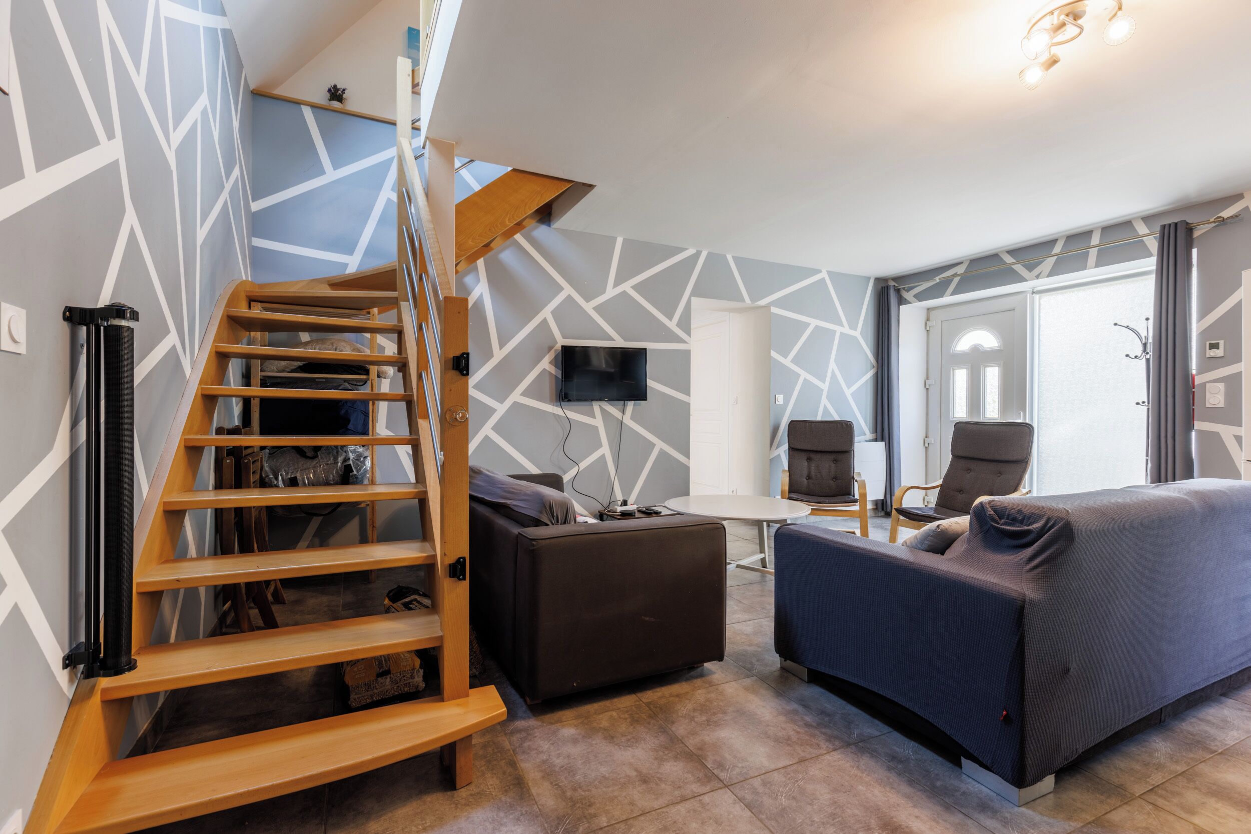 Ein modernes Wohnzimmer mit einer Holztreppe, einem Sofa, einem Fernseher und einem Essbereich.