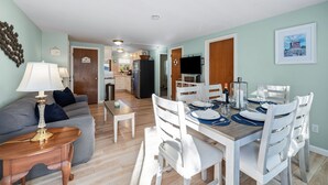 Una sala de estar moderna con un sofá, una mesa de comedor para cuatro comensales y una cocina al fondo.