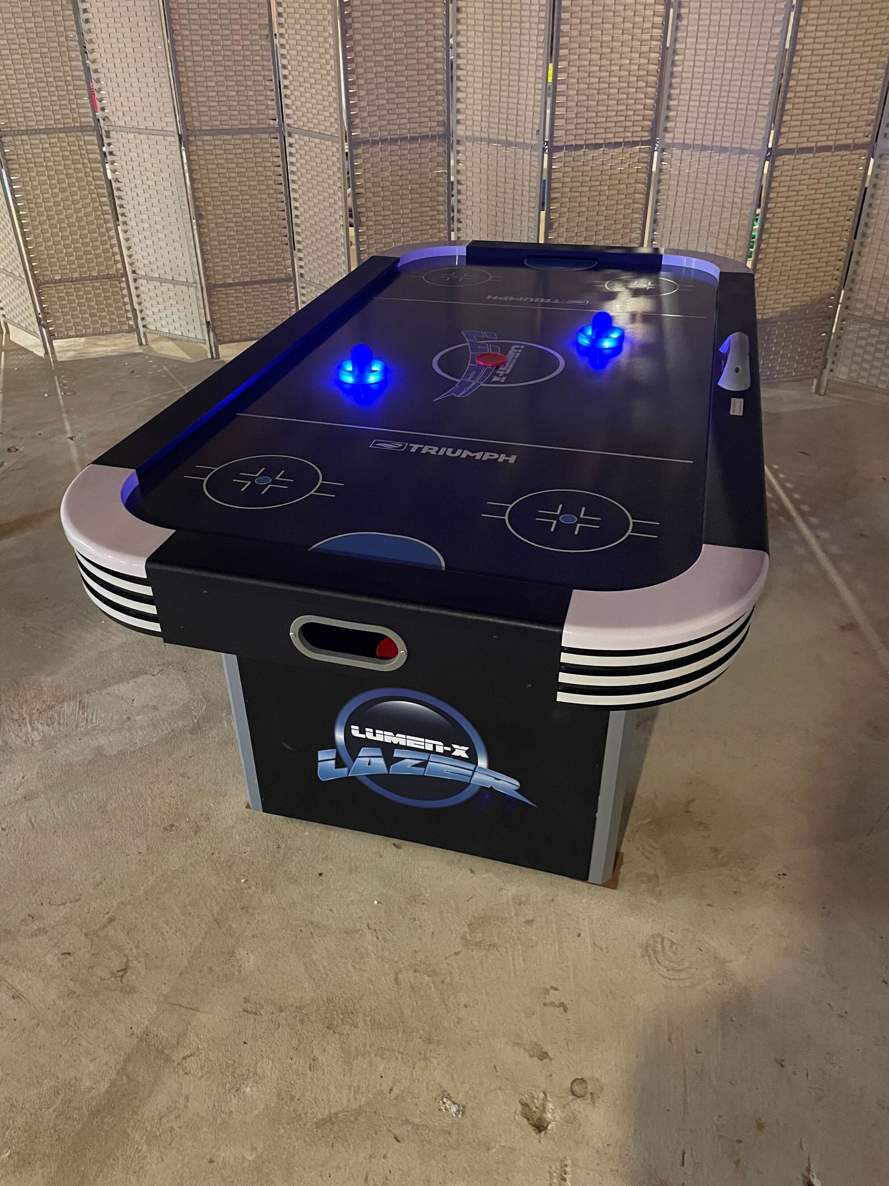Une table de billard avec un plateau noir, orné des logos « TRIUMPH » et « LUMI-X LASER », et dotée de deux boutons rétroéclairés et d’un bouton rouge sur le côté.