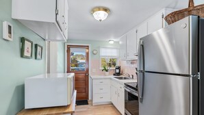 Una cocina compacta con armarios blancos, un refrigerador de acero inoxidable y una encimera de madera.