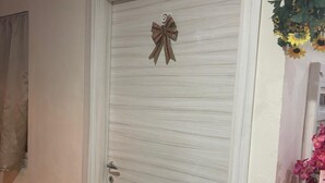 A closed door with a decorative bow, a tiled floor, and a wall-mounted plant with flowers. - Crisan B&b Affittacamere (Nola)