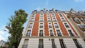 A multi-story building with a brick facade, multiple balconies, and a clear sky. - Superb Apartment Sacre Coeur With Air-conditionner (Paris)