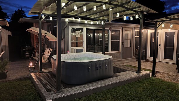 A hot tub under a covered patio with a pergola, surrounded by a backyard with a lawn and a brick wall. - Charming 3-bedroom 5 Bed house with WiFi & extras in delightful Geneva (Geneva)