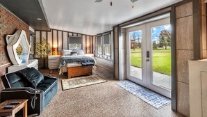 A bedroom with a bed, bedside tables, a dresser, a sofa, and a large window with a view of the outdoors. - Charming 3-bedroom 5 Bed house with WiFi & extras in delightful Geneva (Geneva)