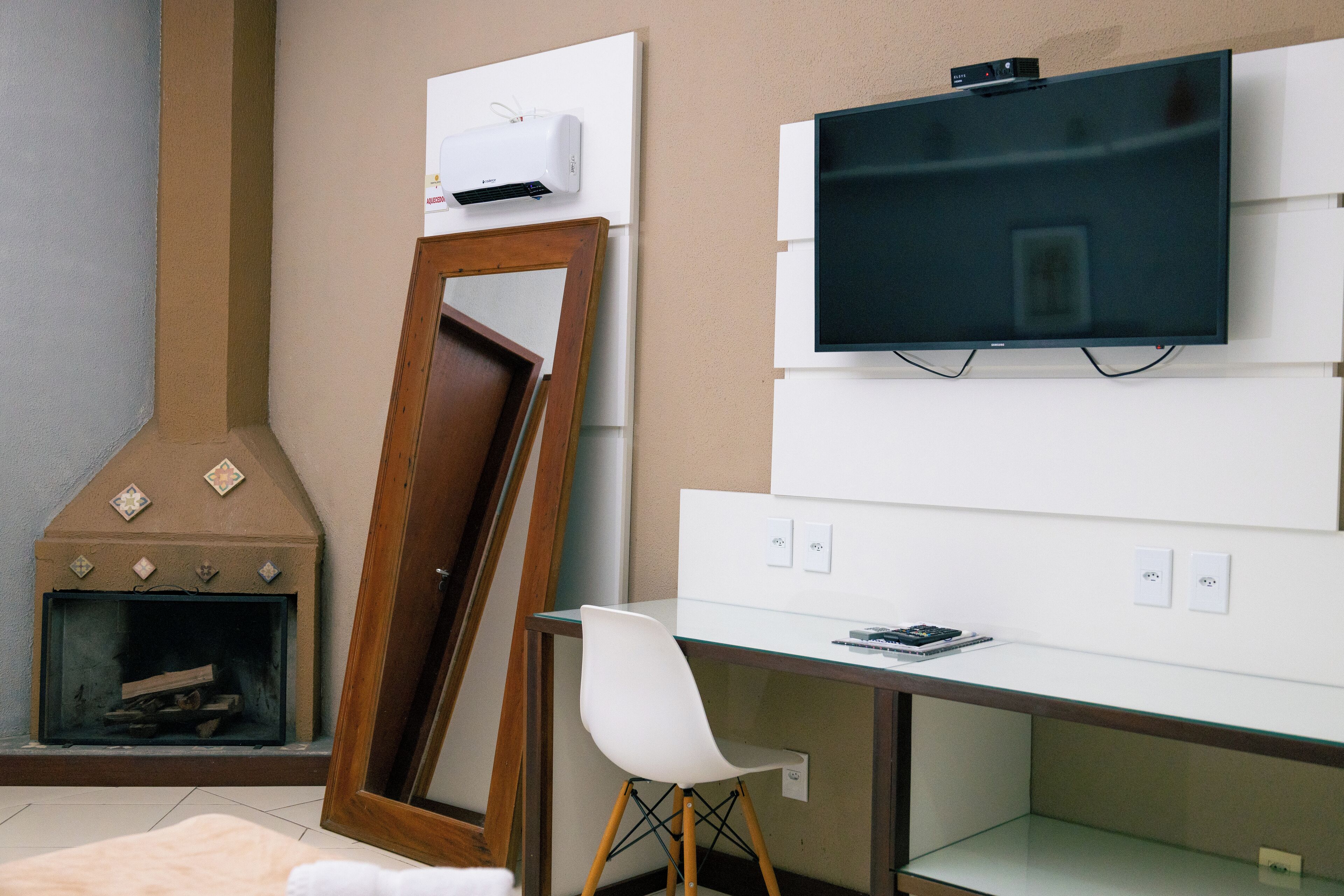 Ein Zimmer mit Kamin, einem an der Wand befestigten Fernseher, einem Schreibtisch und einem Sessel.