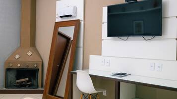 Ein Zimmer mit Kamin, einem an der Wand befestigten Fernseher, einem Schreibtisch und einem Sessel.