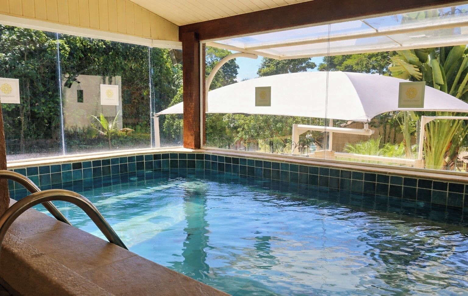 Una piscina con acqua cristallina e azzurra, circondata da una zona coperta che si affaccia sul verde circostante.