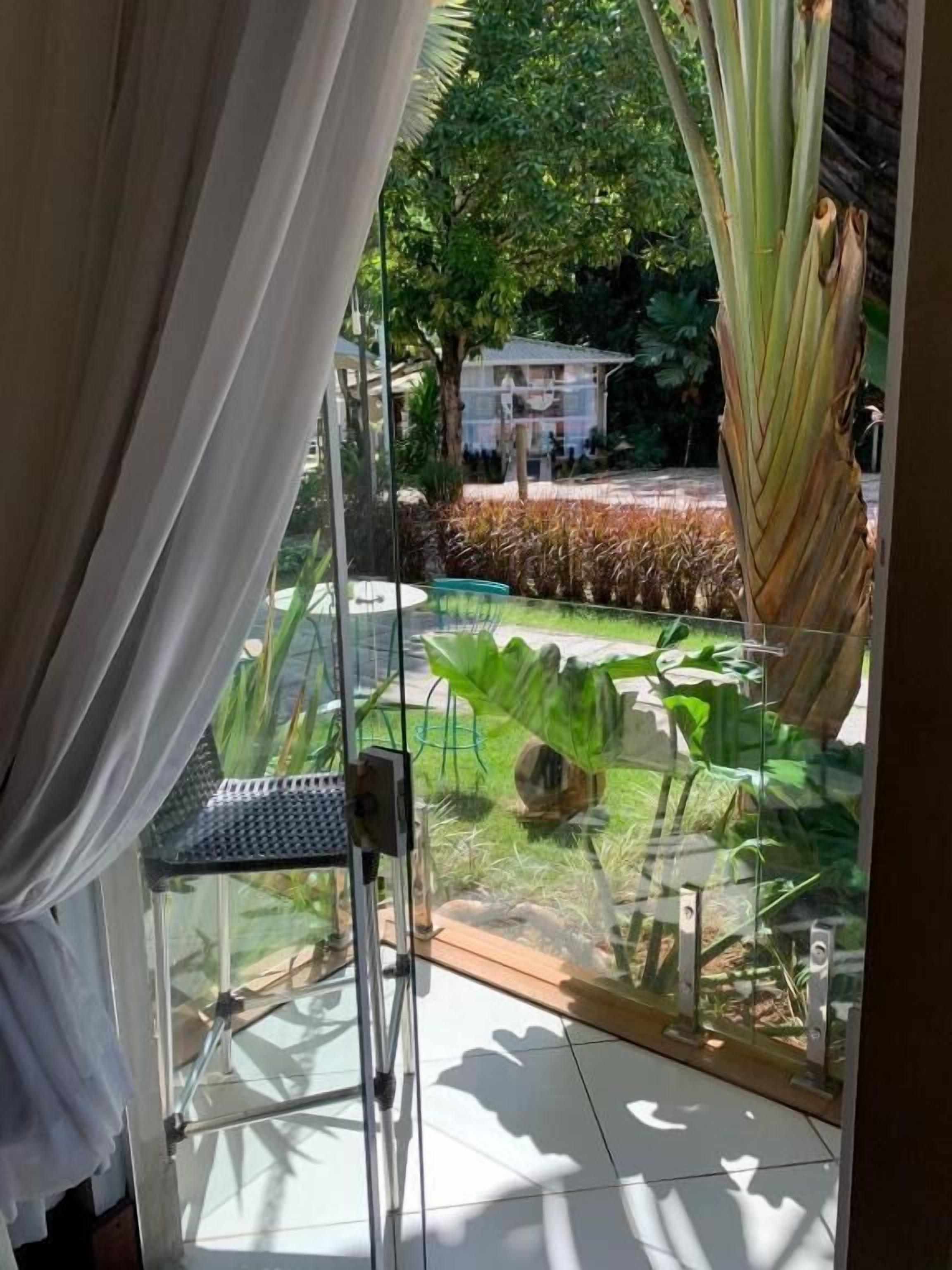 Uma estrutura de vidro com vista para um jardim, uma cadeira de metal e uma mesa de vidro.