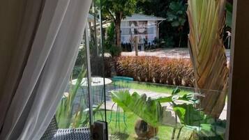 Uma estrutura de vidro com vista para um jardim, uma cadeira de metal e uma mesa de vidro.