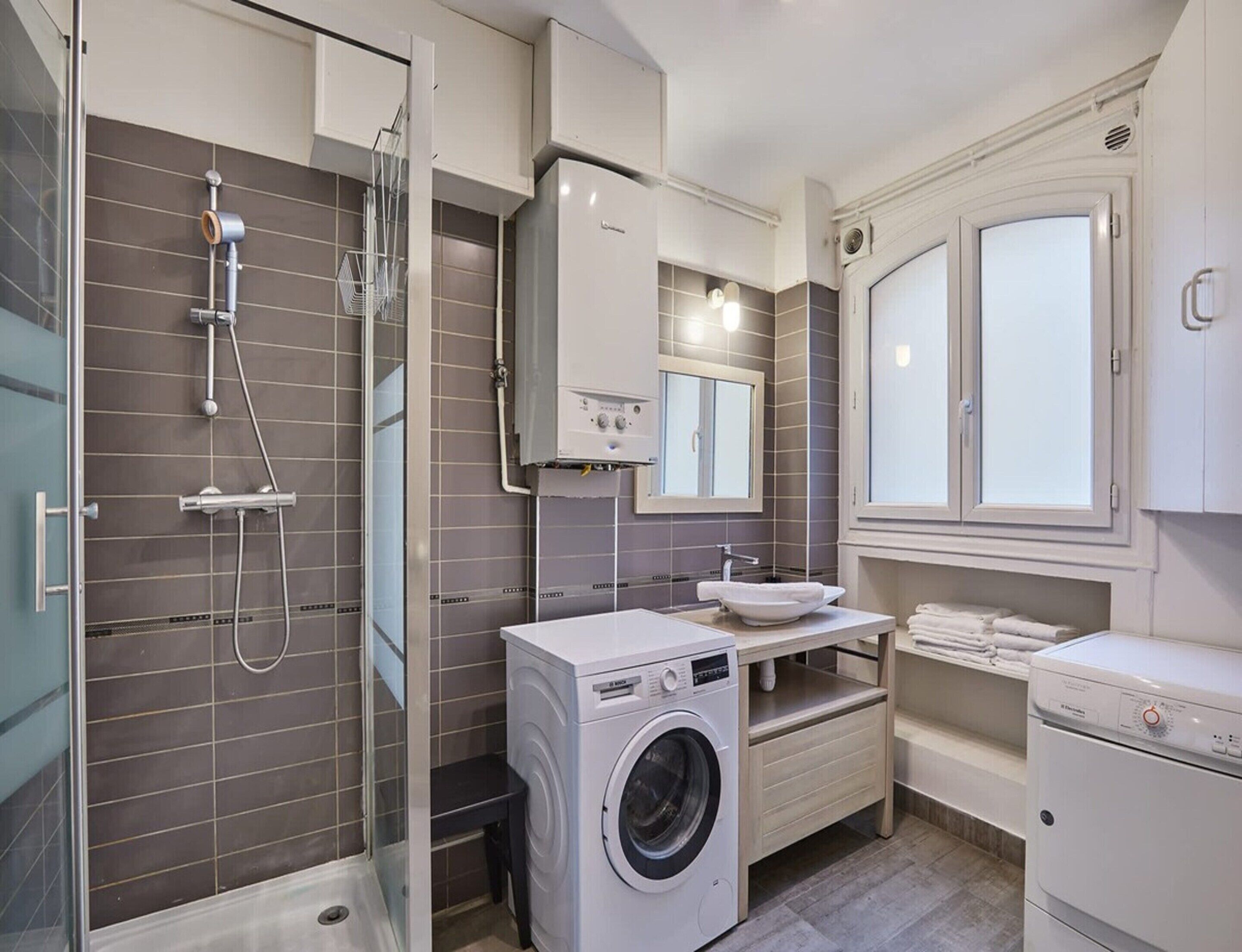 A compact bathroom with a shower, a washing machine, a sink, and a toilet.