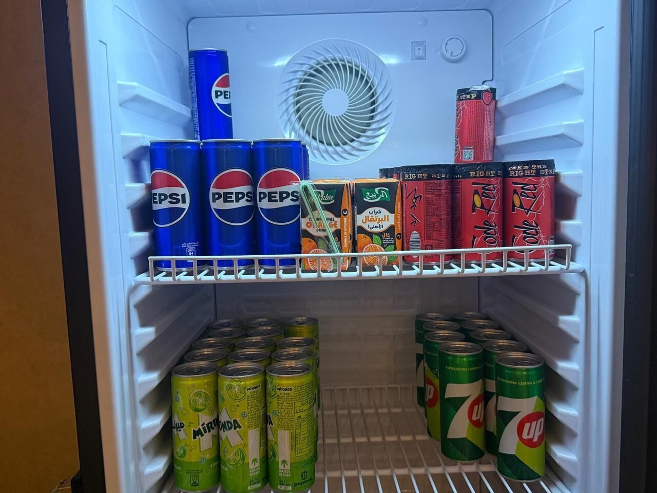 Un réfrigérateur rempli de diverses boissons, notamment du Pepsi, du jus d’orange et du 7UP.