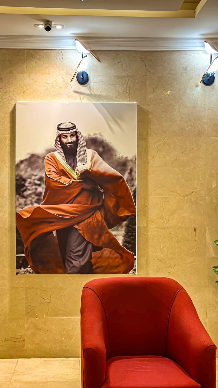 A room with a large poster of a person in traditional attire, a red armchair, and a textured wall.