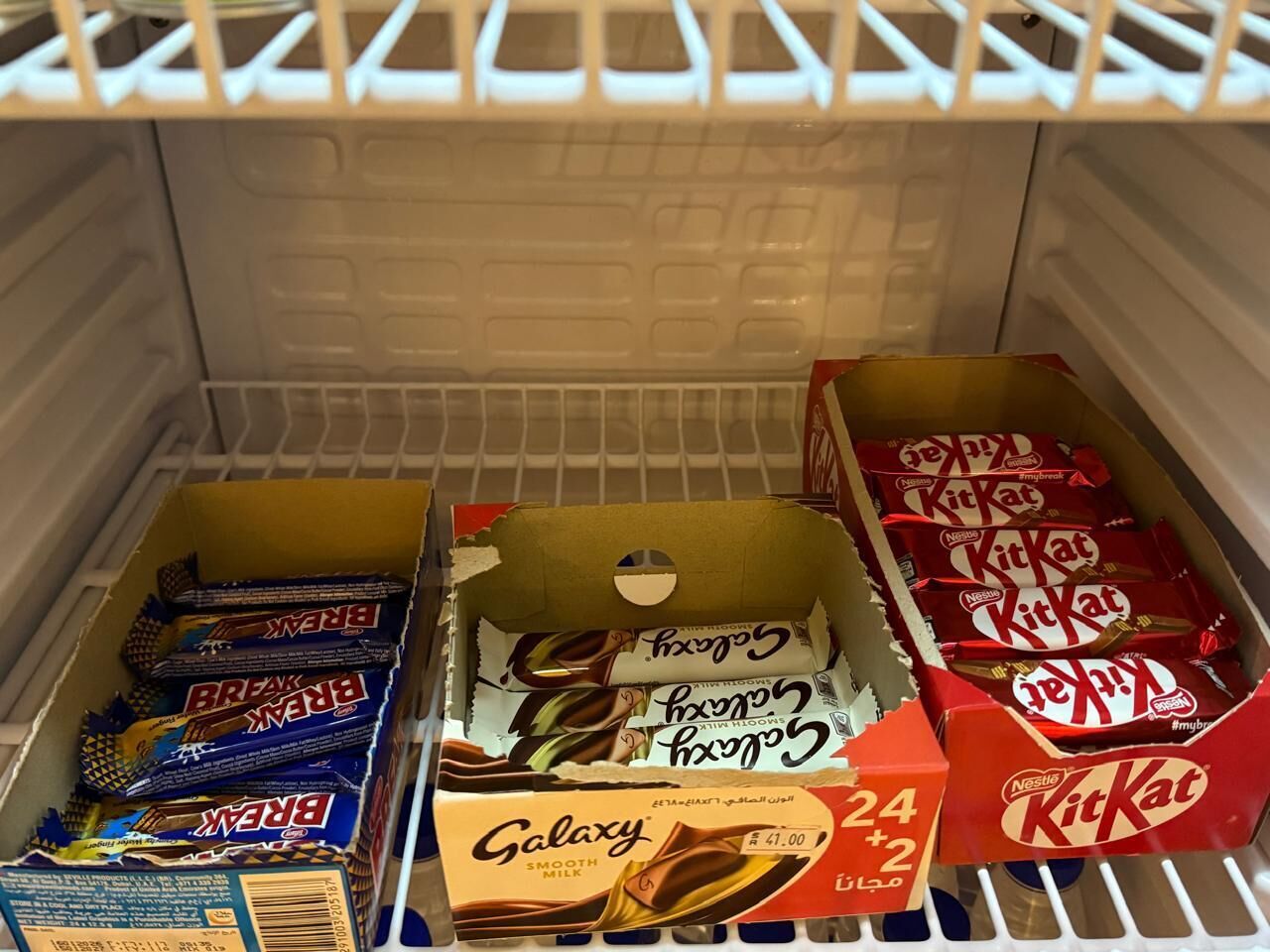 A refrigerator containing multiple boxes of Nestle KitKat and Galaxy chocolate bars.