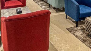 Eine moderne Lobby mit roten und blauen Sesseln, einem grauen Sofa und einem großen Gemälde an der Wand.