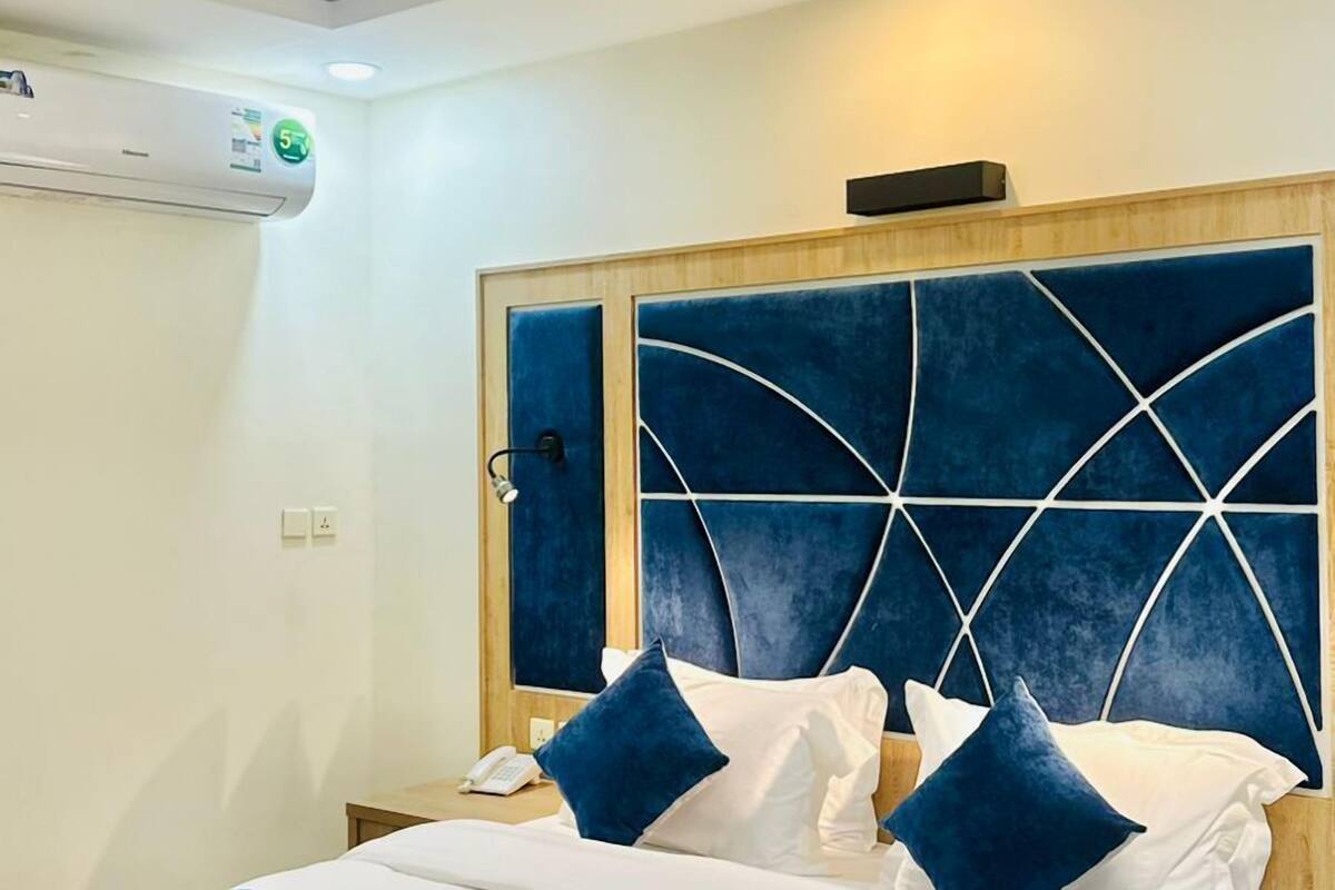 A modern hotel room with a large bed, a wooden headboard with a geometric design, and a bedside table with a lamp.