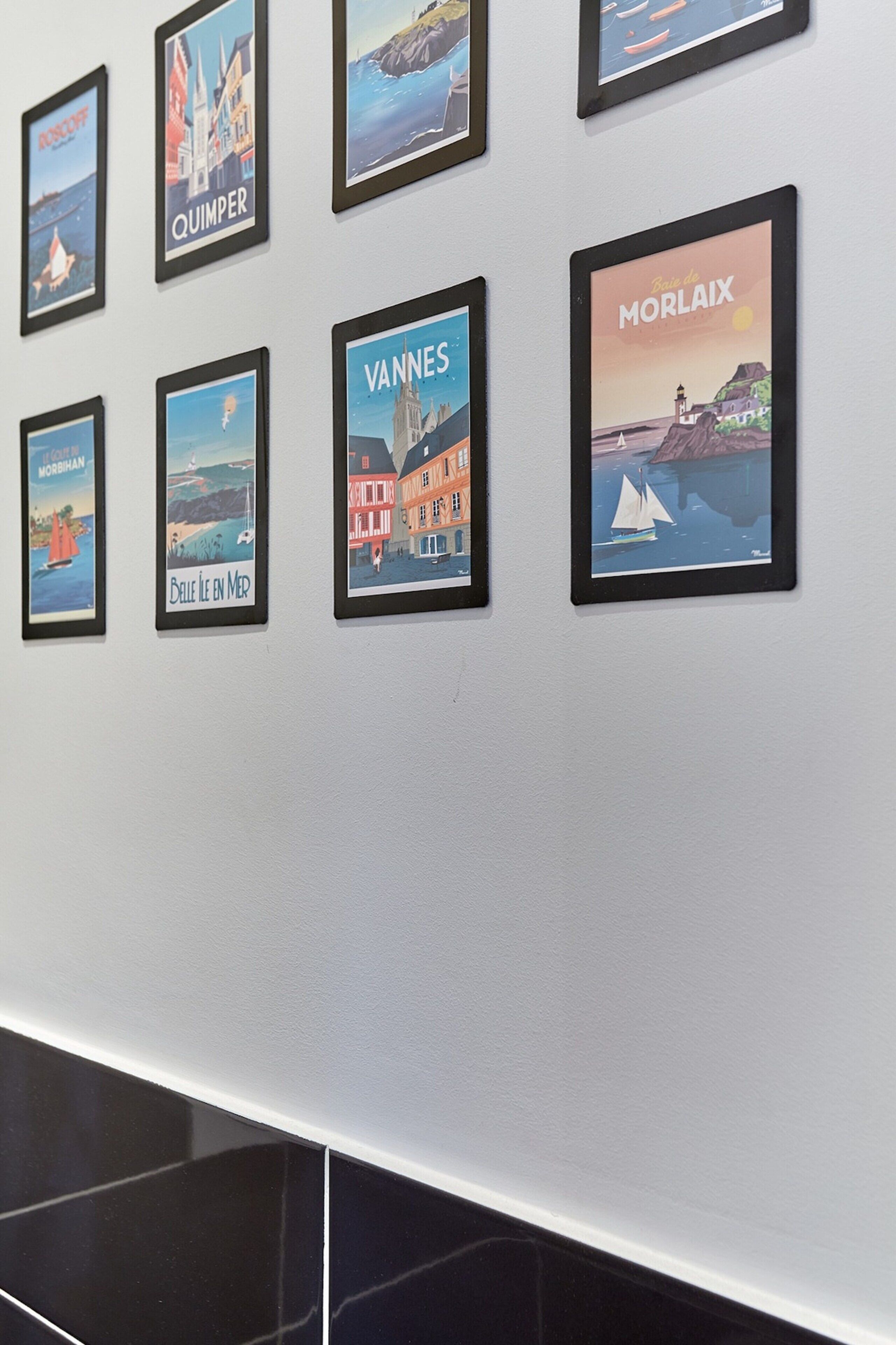 Pared con carteles enmarcados de diversas escenas costeras, incluyendo pueblos como Quimper y Vannes.