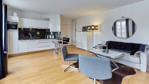 Una cocina moderna con armarios blancos, un comedor con mesa y sillas, y una sala de estar con sofá y espejo.