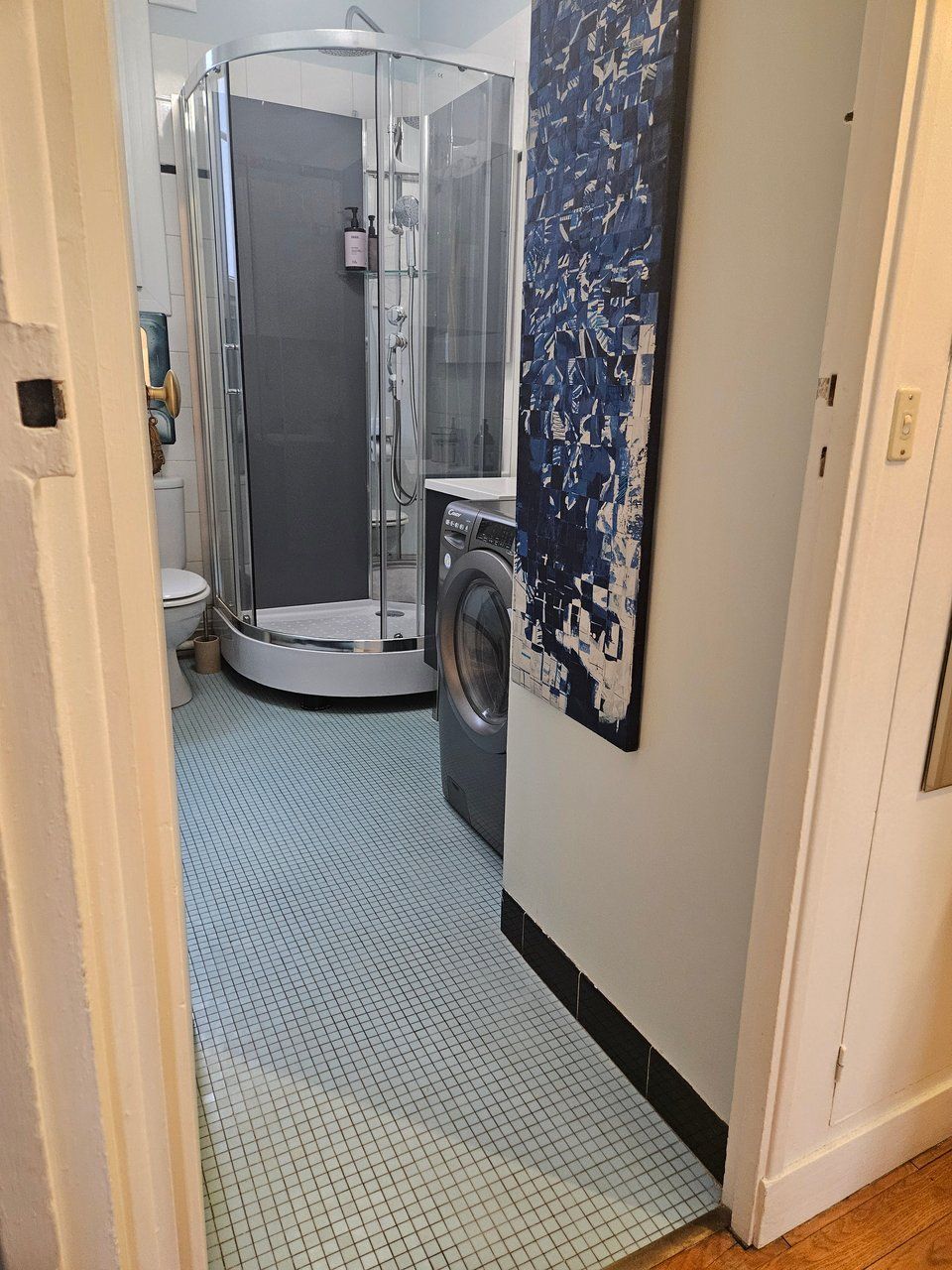 A bathroom with a glass-enclosed shower, a washing machine, and a tiled floor.