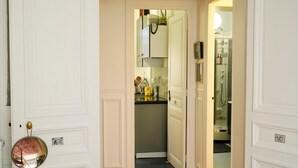 A hallway leading to a bathroom with a mirror, a clock, and a small kitchen area.