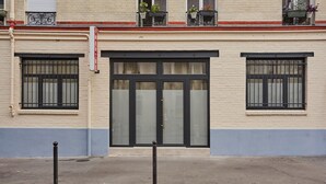 A building facade with a large central door, two windows on either side, and a red sign above the door. - Exceptional Apartment Near Montmartre 10 People (Paris)