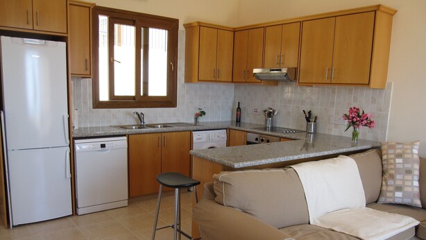 A kitchen with wooden cabinets, a refrigerator, a dishwasher, and a bar stool. - Peyia, near Paphos, Cyprus - beautiful villa with panoramic view over coral bay  (Peyia)