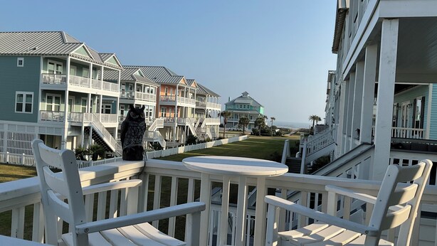 A balcony with white railings and a view of multi-story buildings with balconies and a lawn.