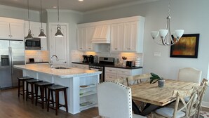 A modern kitchen with white cabinetry, a central island with stools, and a dining area with wooden chairs and a table.