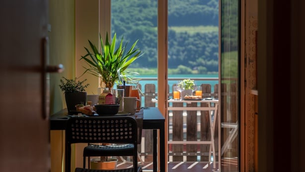 Een eetgedeelte met een tafel gedekt voor twee personen, een potplant en uitzicht op een bergachtig landschap door een glazen deur.