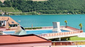 A view of a lake with a mountain in the background, a swimming pool area, and a building with a red roof.