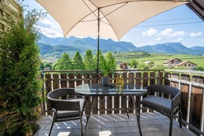 Un balcon avec une table, deux chaises et un grand parasol.